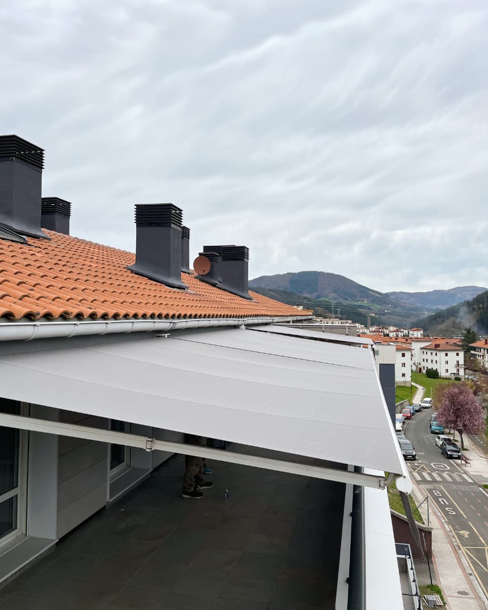 Toldo hedagarri grisa, teilatu laranja duen atikoko terraza batean instalatua, Itzalki Toldoak enpresak Zarautzen (Gipuzkoa, Euskal Herria) egindakoa, Bergaran ere zerbitzua eskaintzen duena