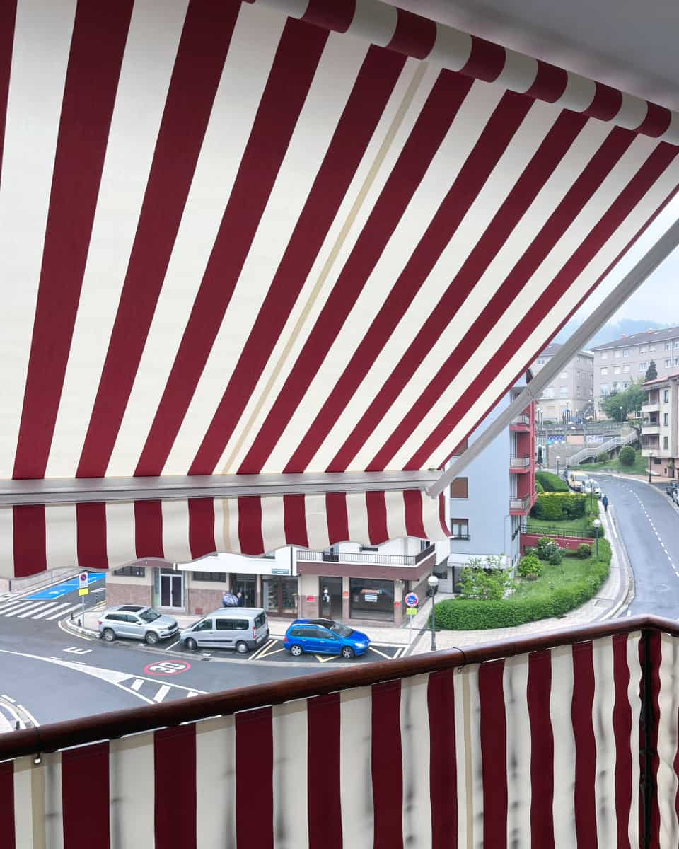 Marra gorri eta zuriak dituen toldo hedagarria, hiri-eraikin bateko balkoian instalatua, Itzalki Toldoak enpresak Zarautzen (Gipuzkoa, Euskal Herria) jarritakoa, Tolosan ere zerbitzua eskaintzen duena